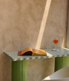 an open book sitting on top of a green table next to a glass of wine