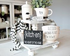 a white table topped with cups and saucers next to a sign that reads kitchen the heart of the home