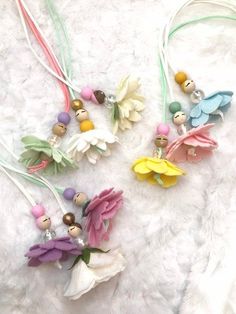 four little angel necklaces on a white furnishing with flowers and beads hanging from them