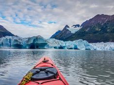 a red kayak in the water with icebergs and mountains in the background