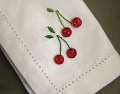 three cherries are embroidered onto the back of a white linen pocket with stitching