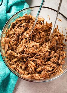 a glass bowl filled with shredded meat sitting on top of a blue towel next to a fork