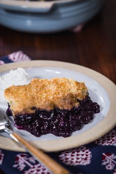 a piece of blueberry cobbler on a plate with whipped cream and spoons