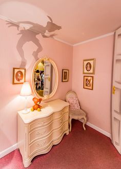 a room with pink walls and pictures on the wall, including a dresser and mirror