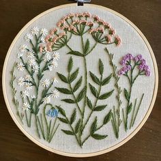 a close up of a embroidery on a wooden surface with flowers in the center and leaves around it