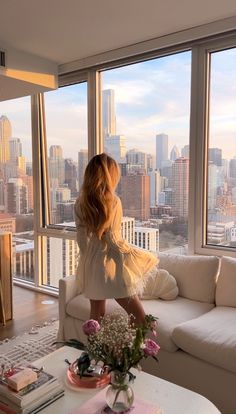 a woman standing in front of a large window looking out at the city from her living room