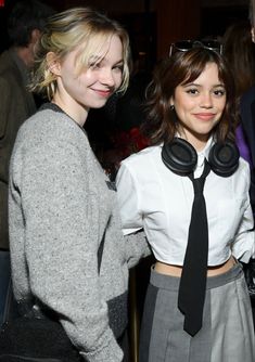 two women standing next to each other with headphones on their ears and one wearing a tie