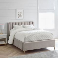 a bed with white sheets and pillows in a room next to a window, side table