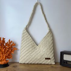 a white knitted bag hanging on a wall next to a radio and potted plant