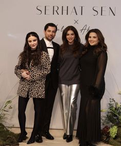 three women and one man standing next to each other in front of a white wall