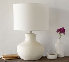a white vase sitting on top of a wooden table next to a lamp and book