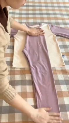 a woman holding onto a purple shirt on top of a checkered tablecloth covered bed