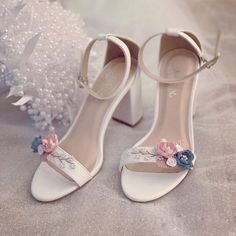 a pair of white high heels with flowers on the side and pearls in the background
