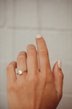 a woman's hand with a diamond ring on her left hand and a white brick wall in the background