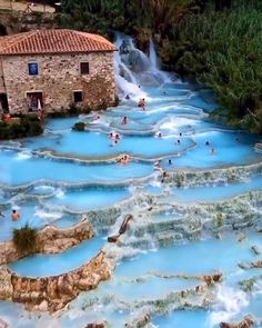 people are swimming in the blue water near an old building and waterfall with stone walls