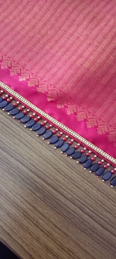 a pink and blue sari with tassels on the edge is laying on a wooden surface