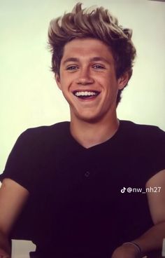 a smiling young man sitting in front of a white wall