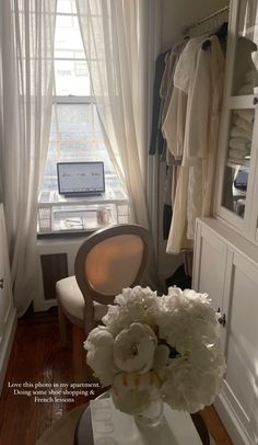 there is a vase with flowers in front of the window and a laptop on the desk