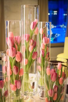 pink tulips in clear vases sitting on a table with other glass vases