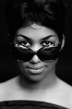 a woman with sunglasses on her face is posing for the camera in front of a black background