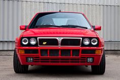 a red car parked in front of a metal building with it's hood up