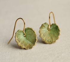 a pair of green and gold earrings with leaves on them sitting on a white surface