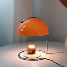 an orange table lamp sitting on top of a white table next to a lit candle