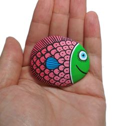 a hand holding a small rock with a fish painted on it's face and eyes