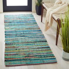 a colorful rug is on the floor next to a chair and potted plant in a white room