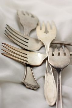four forks and two spoons are arranged on a white table cloth with silverware