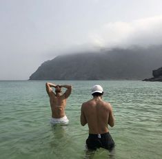 two men standing in the water with their backs to each other and one man wearing a white hat