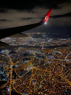 an airplane wing flying over a city at night with lights on the ground and in the air