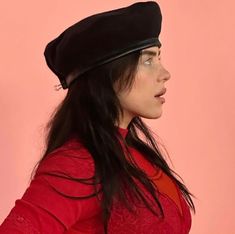 a woman with long hair wearing a black beret and red shirt against a pink background
