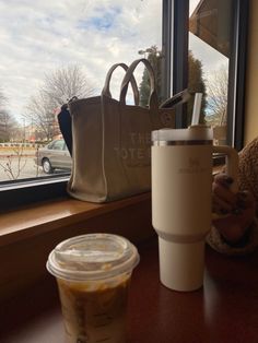 a cup of coffee next to a bag on a window sill with a woman looking out the window