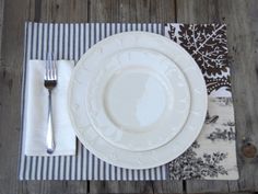 a white plate with a fork and knife on top of a striped place mat next to a wooden table