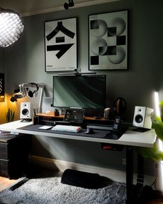 a computer desk with speakers and a laptop on it in front of two framed pictures