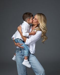 a woman kissing a young boy on the cheek while he is wearing jeans and a white shirt