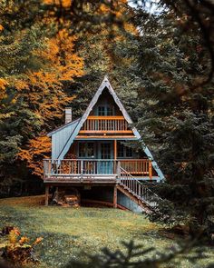 a cabin in the woods surrounded by trees with fall leaves on it's branches