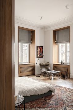 a bed sitting in a bedroom next to two windows and a rug on the floor