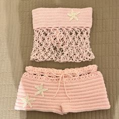 two pieces of pink crocheted clothing sitting on top of a bed