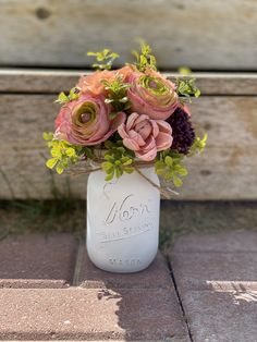 a mason jar filled with flowers sitting on top of a brick floor next to a wooden bench