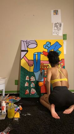 a woman is sitting on the floor in front of a colorful art piece and painting