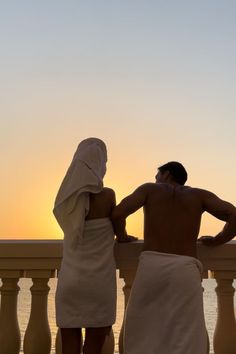 two people standing on a balcony looking out at the ocean with their backs to each other