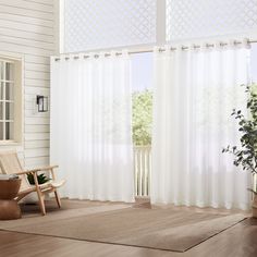 a living room with white curtains and a chair in front of the window, next to a potted plant