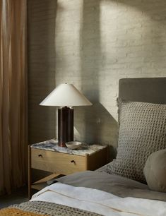 a bed with a lamp on top of it next to a night stand and window