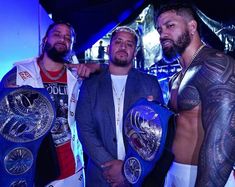 three men standing next to each other holding wrestling belts