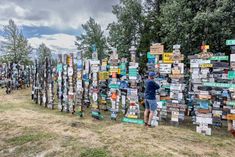 a man standing next to a wall covered in lots of different colored signs and trees