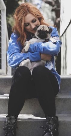 a woman sitting on steps holding a small pug dog in her arms and looking at the camera