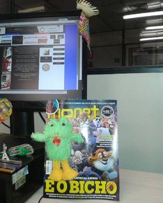 a stuffed animal sitting in front of a computer monitor on a desk next to a magazine