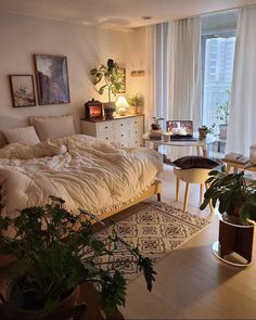 an unmade bed sitting next to a window in a room with potted plants